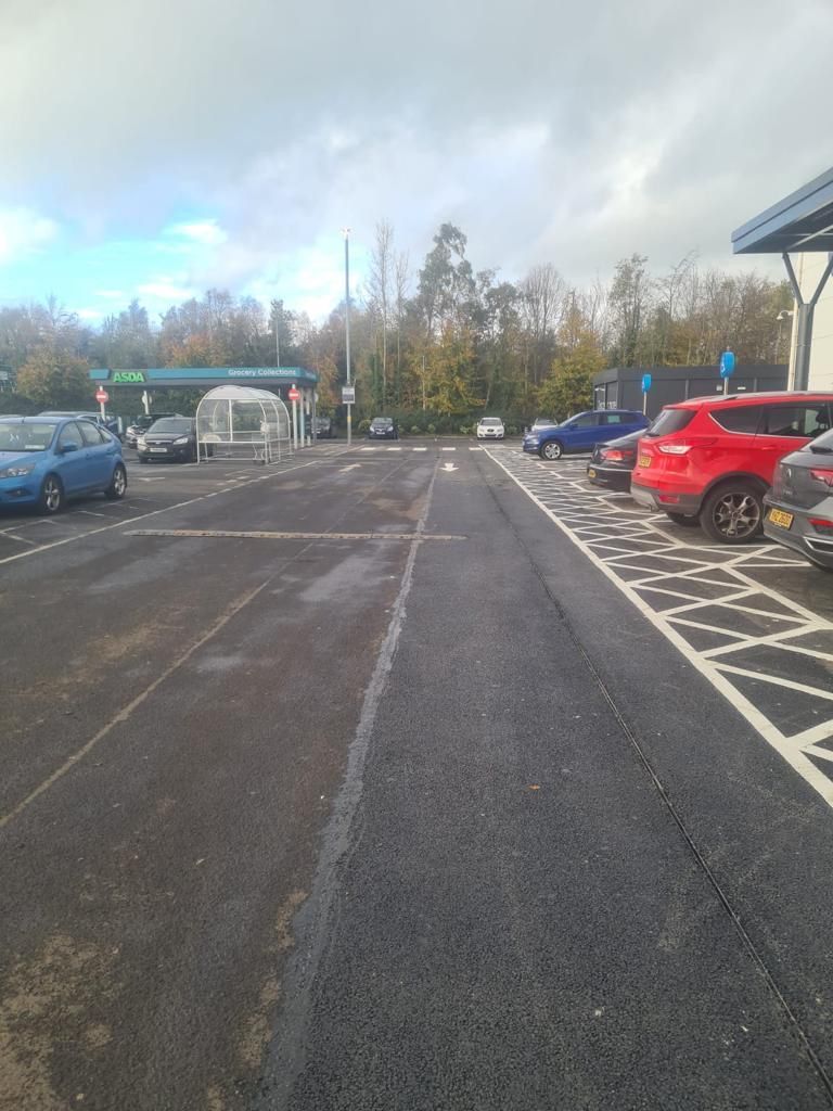 Car park access road with fresh hatching and white lining, cars parked beyond.