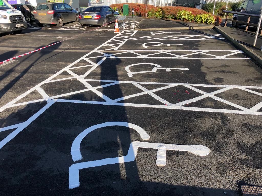 Newly marked disabled bays with hatching and access markings on fresh black asphalt.