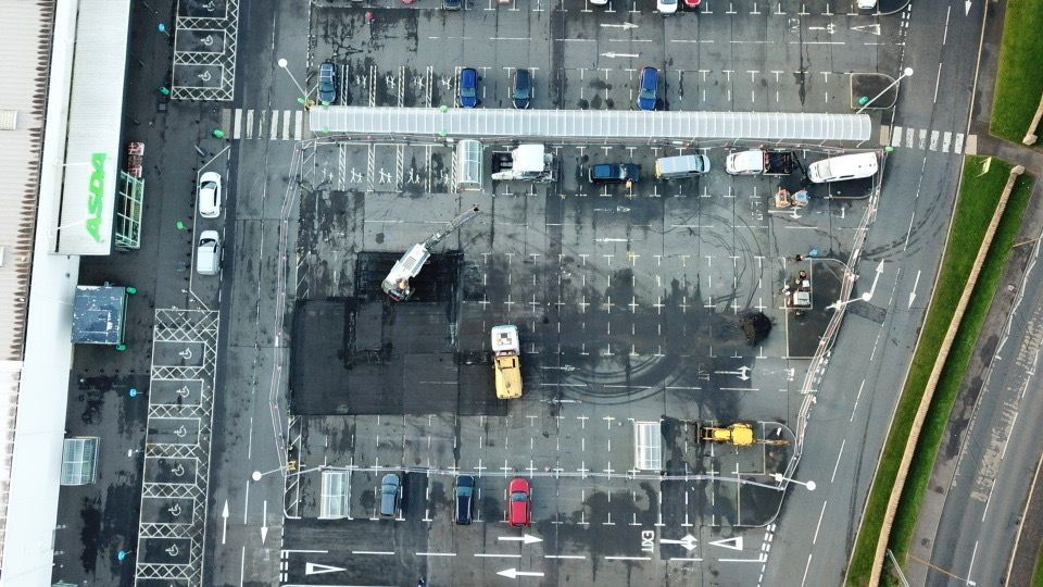 Overhead view of the resurfaced access road with a roller working and traffic arrows relaid.