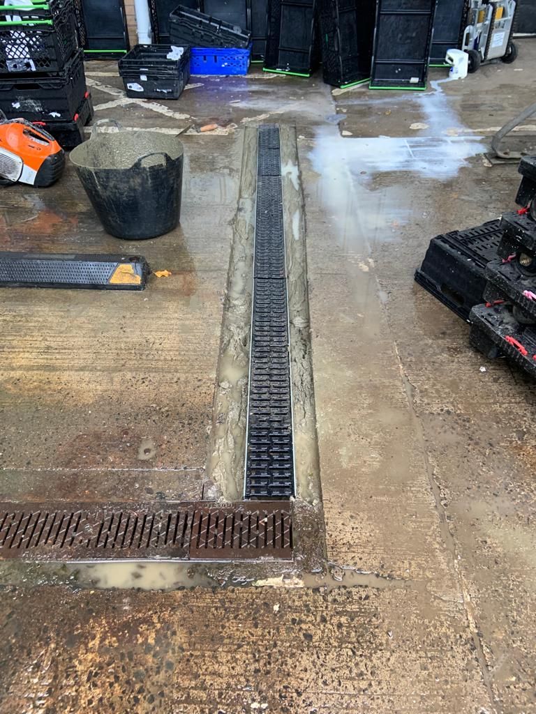 New slot drainage channel run along the yard wall beside stacked delivery crates.