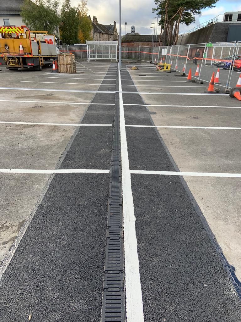 New slot drainage channel set into fresh asphalt between white bay markings in a supermarket car park.