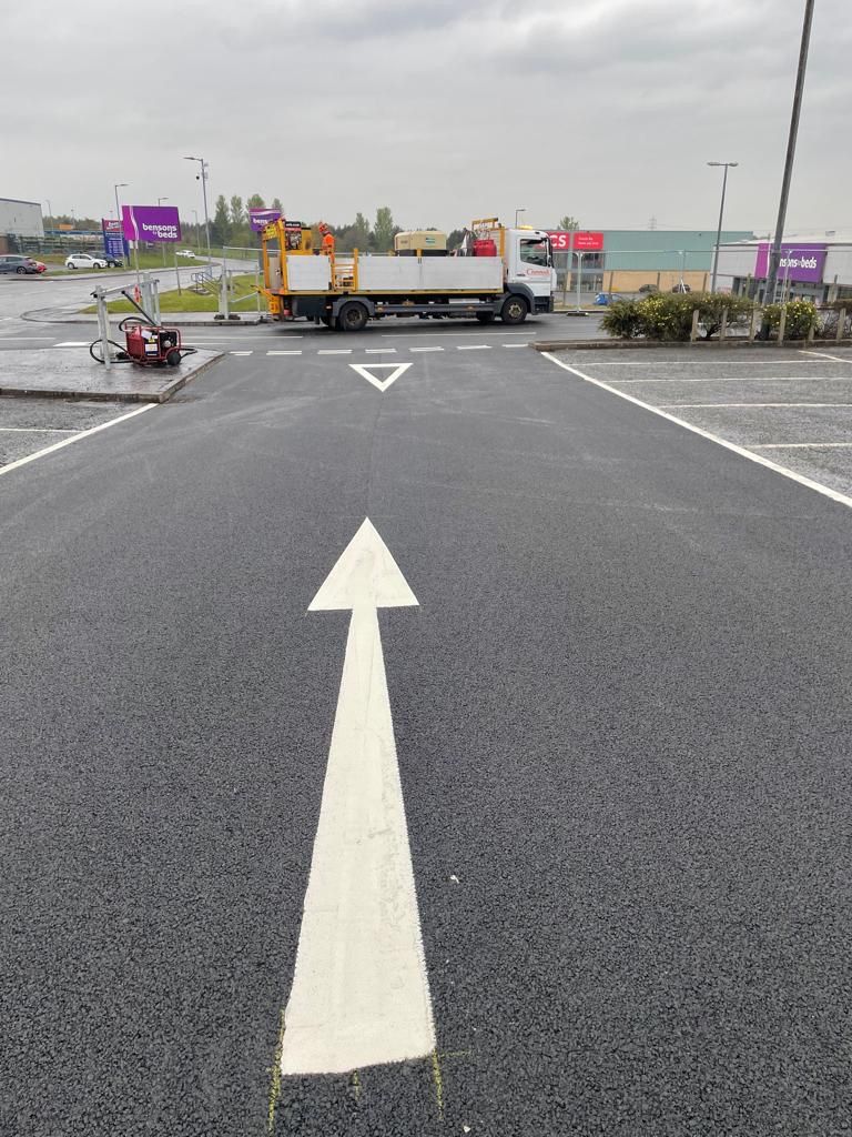 Large white directional arrow freshly laid on the resurfaced car park.